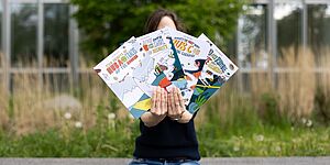 Person holding up the four English-language CASA science comics