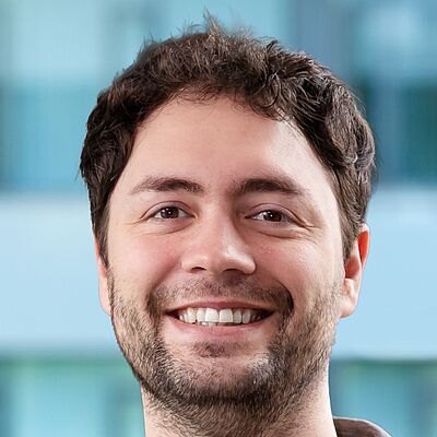 Porträt eines Mannes mit kurzem, lockigem Haar und Bart vor unscharfem Hintergrund. Es handelt sich um Jonas Haferkamp.