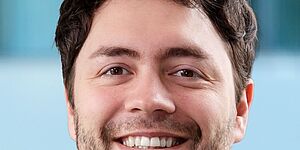 Porträt eines Mannes mit kurzem, lockigem Haar und Bart vor unscharfem Hintergrund. Es handelt sich um Jonas Haferkamp.