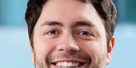 Porträt eines Mannes mit kurzem, lockigem Haar und Bart vor unscharfem Hintergrund. Es handelt sich um Jonas Haferkamp.