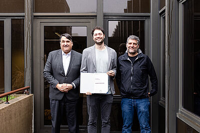 Rektor Prof. Dr. Martin Paul, Jonas Haferkamp und Dekan Prof. Dr. Gregor Leander beim Verleih der Professur.