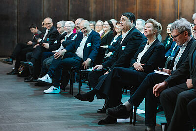 Das Publikum auf Stuehlen darunter Rektor Martin Paul und Ministerin Ina Brandes