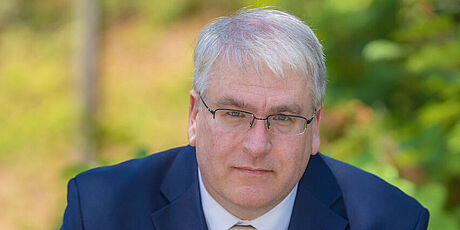 Mann im blauen Anzug vor unscharfem Hintergrund. Es handelt sich dabei um Michael Bailey.