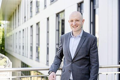 Julian Loss steht im Anzug vor einem Gebäude der Ruhr-Universität Bochum.