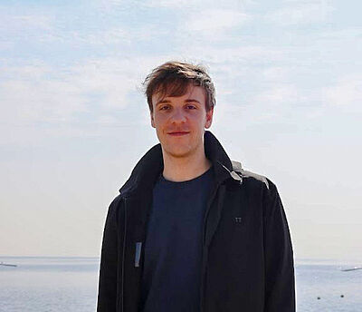 Ein Portrait von CASA PhD Tobias Wienand. Ein Mann mit braunen Haaren steht vor einem hellen Hintergrund.